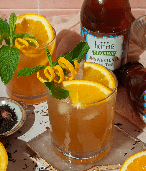 Sparkling Orange Tea Mocktail in a Glass with a Bottle of Heinen's Organic Unsweetened Iced Tea