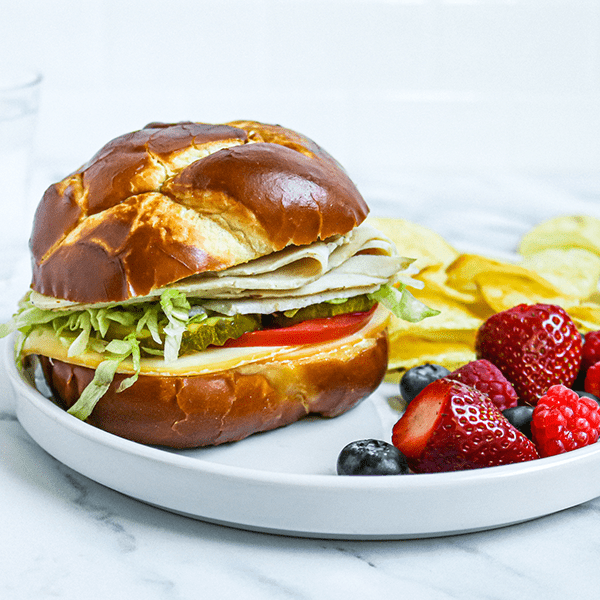 A Turkey Sandwich on a Pretzel Bun on a Plate with Fresh Berries and Potato Chips