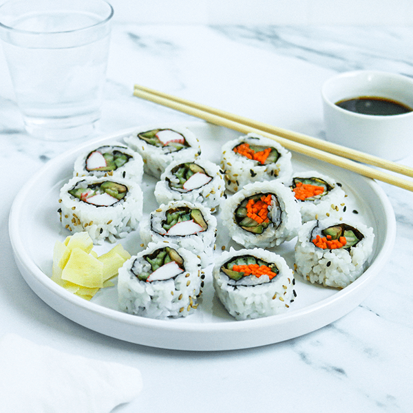 A Serving Plate with Fresh Sushi Rolls, Chop Sticks, Ginger and a Cup of Soy Sauce