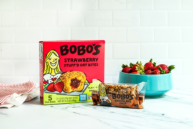 One great after school snack item for your back-to-school grocery list: A box of Bobo's Strawberry Stuff'd Oat Bites and a Chocolate Chip Oat Bar on a white countertop