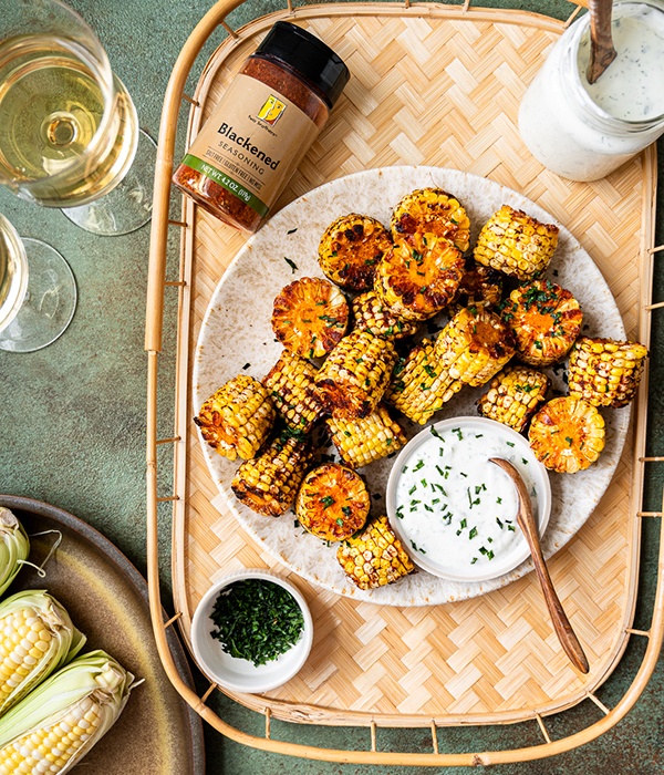Cajun Corn Bites with Greek yogurt ranch sauce served on a plate, and placed on a woven wooden tray