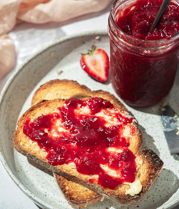 A piece of toast slathered with Homemade Strawberry Fruit Preserve and butter on a plate