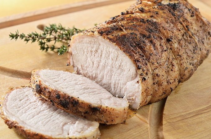 Herb crusted quality pork tenderloin roast being sliced on a cutting board