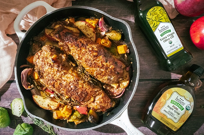 Maple Garlic Marinated Pork Tenderloin with Fall Vegetables in a pan with a bottle of Heinen's Maple Syrup and Heinen's Extra Virgin Olive Oil