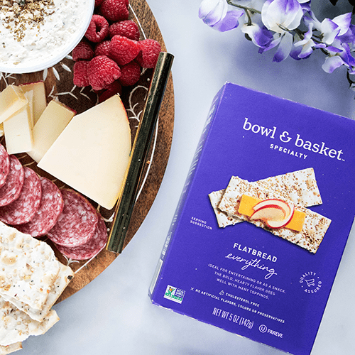 A Cheese and Charcuterie Board Beside a Box of Bowl & Basket Everything Flatbread Crackers