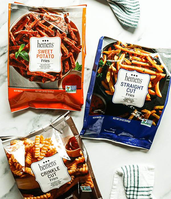 Bags of Heinen's Frozen Sweet Potato Fries, Heinen's Frozen Straight Cut Fries, and Heinen's Crinkle Cut Fries on a White Surface