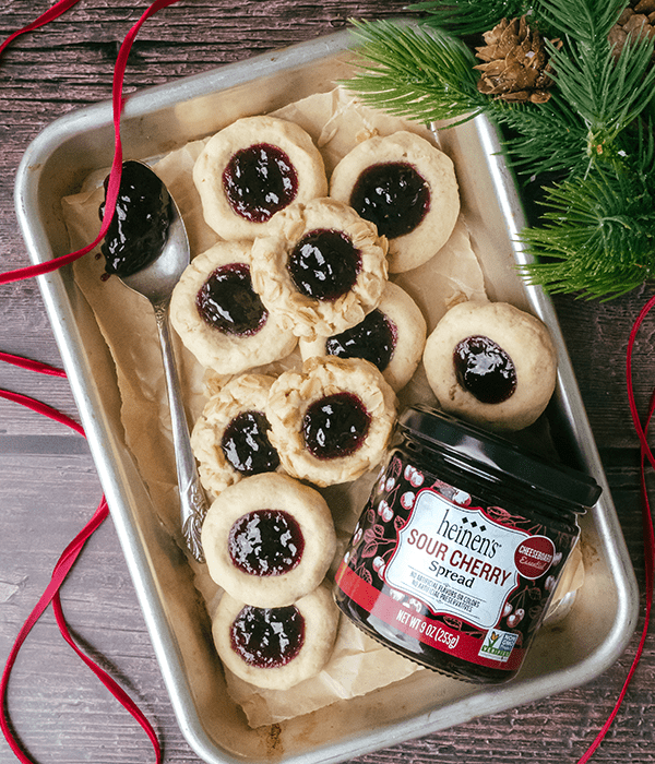 Sour Cherry Thumbprint Cookies on a Parchment-Lined Baking Sheet Beside a Jar of Heinen's Sour Cherry Spread