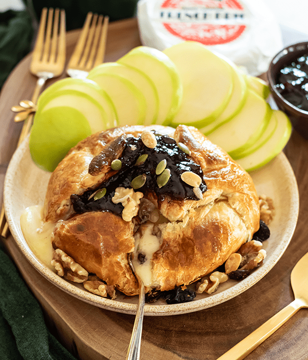 Baked Brie en Croute Topped with a Fruit Spread and Nuts and Served on a Plate with Fresh Sliced Apples