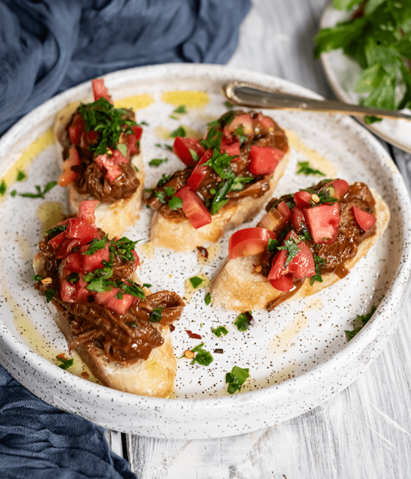 A Serving Plate with Four Pieces of Brisket Bruschetta Drizzled in Olive Oil