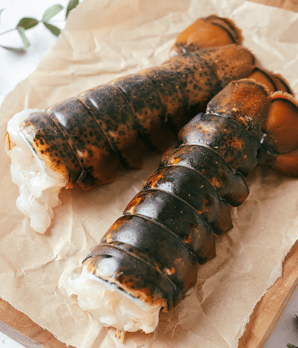 Two Raw Lobster Tails on Brown Parchment Paper